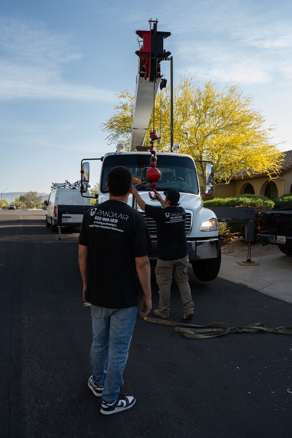 Two Panda Air technicians walking toward the crane truck in a residential street