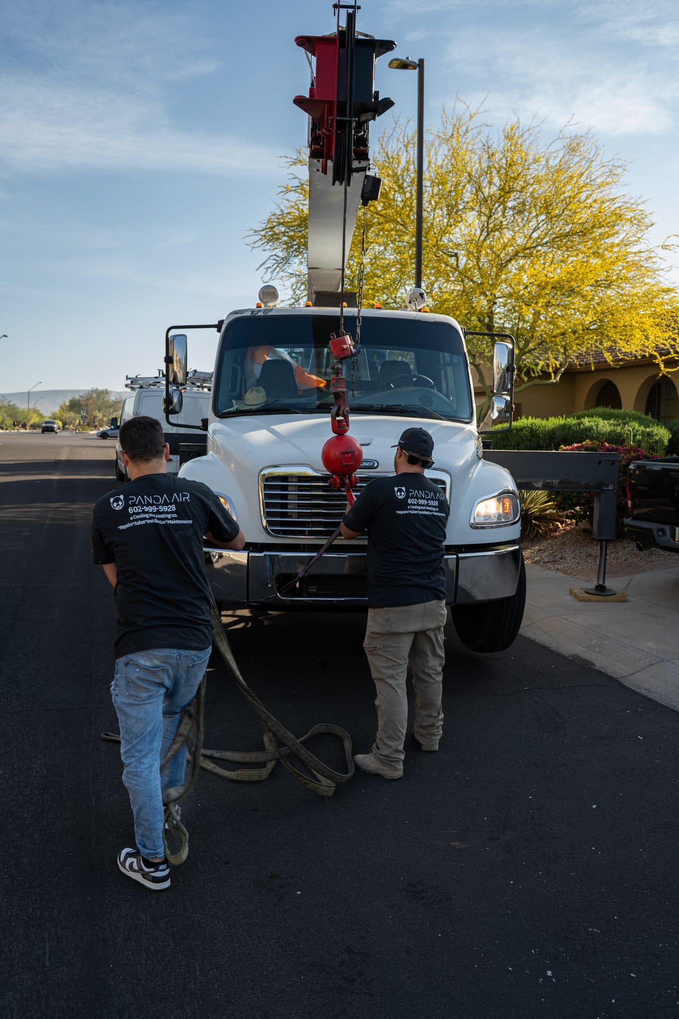 Two Panda Air technicians rigging lifting straps at the front of a crane truck