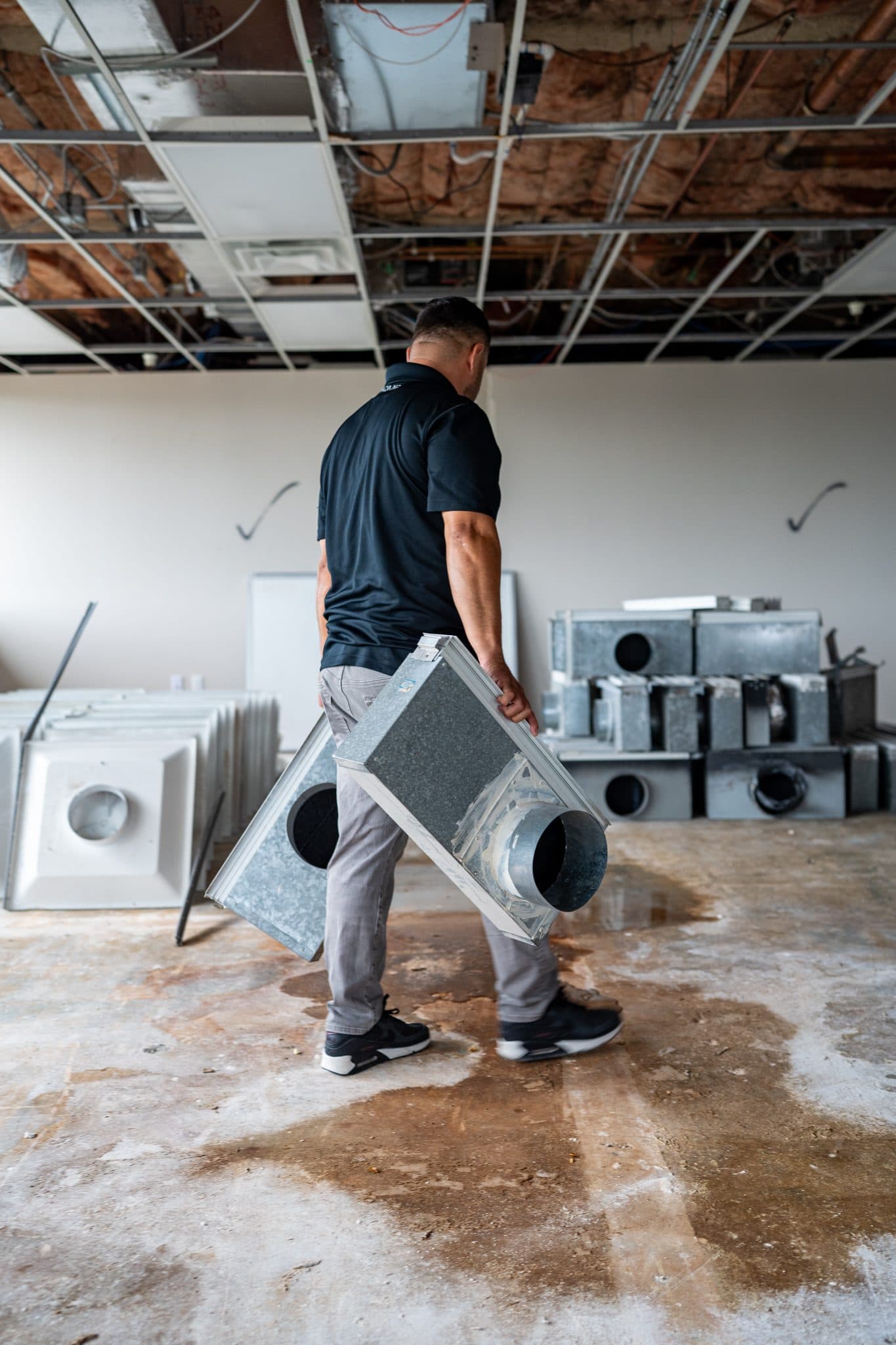 A technician carrying a sheet metal duct boot across a commercial floor
