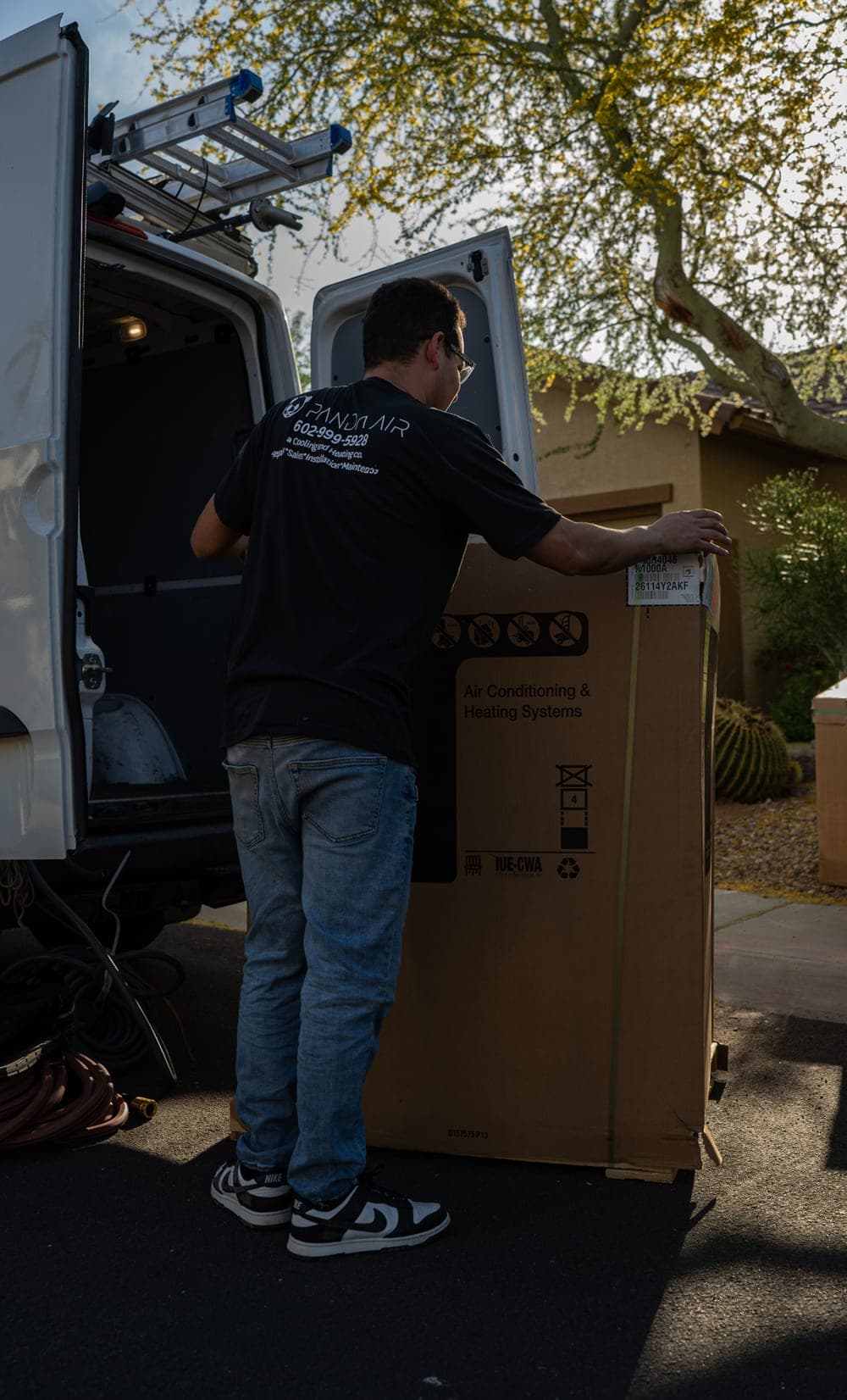 A Panda Air technician standing a boxed air conditioning and heating system upright beside the service van