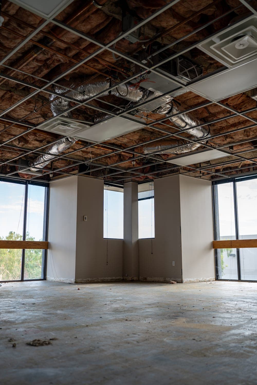An empty office corner with flex duct and air vents in the opened ceiling above