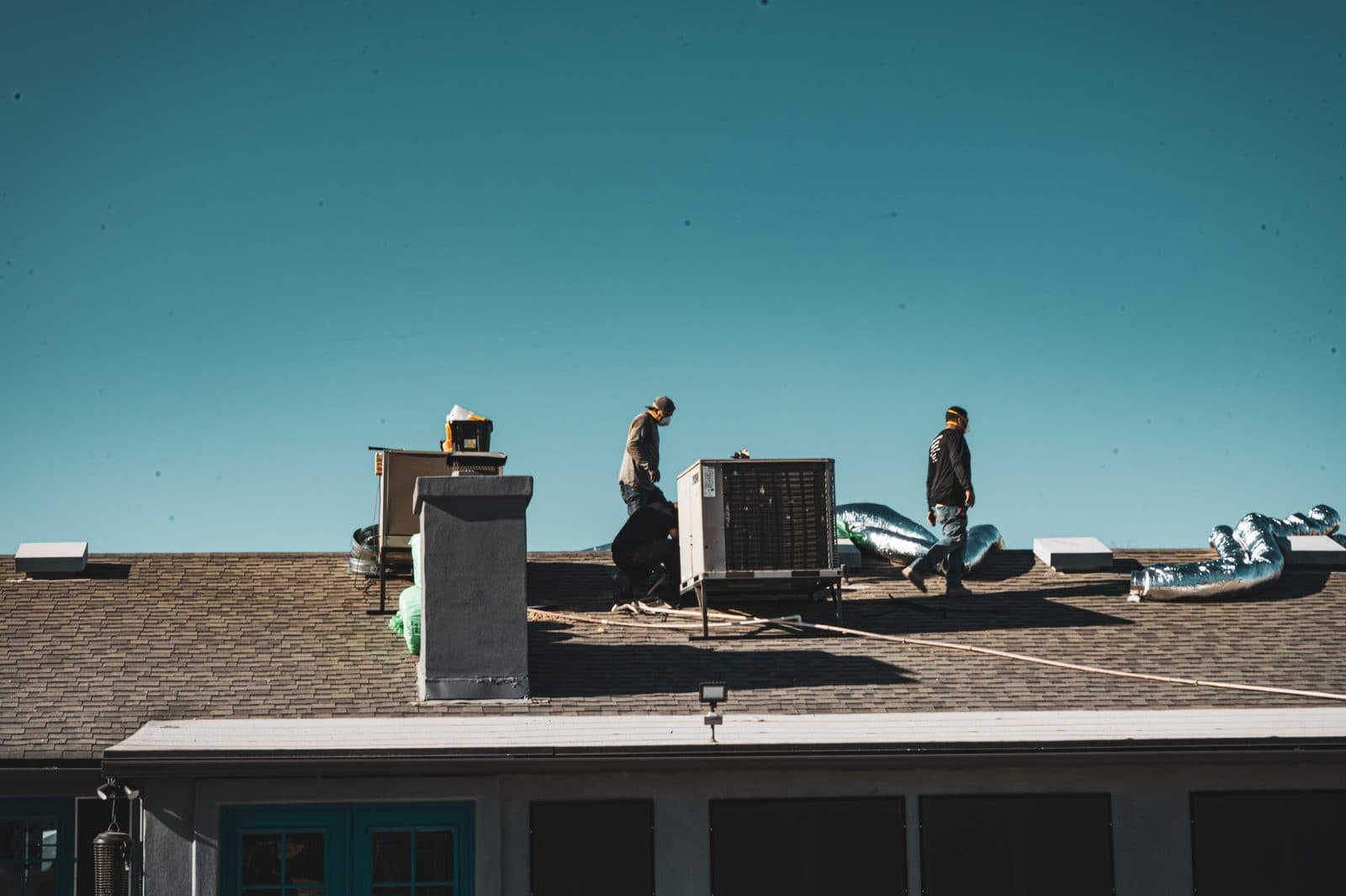 Workers on a roof beside a packaged rooftop unit